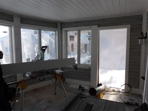 Interior of screened porch conversion with miter saw, sawhorses, new windows, and beadboard ceiling under construction