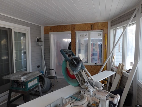 Screened porch conversion with miter saw, OSB wall framing, and new windows being installed in winter