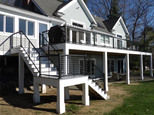 Large multi-level home exterior with elevated white deck, black cable railings, and black metal stairs in spring
