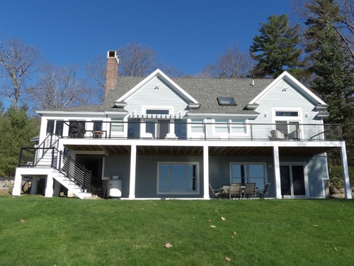 Completed blue-gray home exterior with expansive white lower deck, black cable railings, and upper balcony