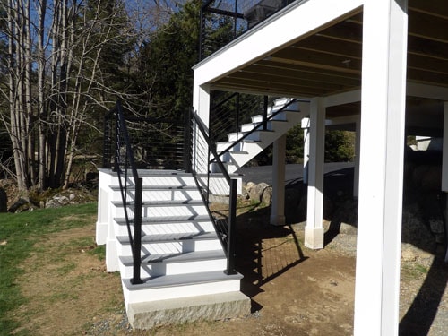 Gray composite deck stairs with black metal railings and white posts under elevated deck structure
