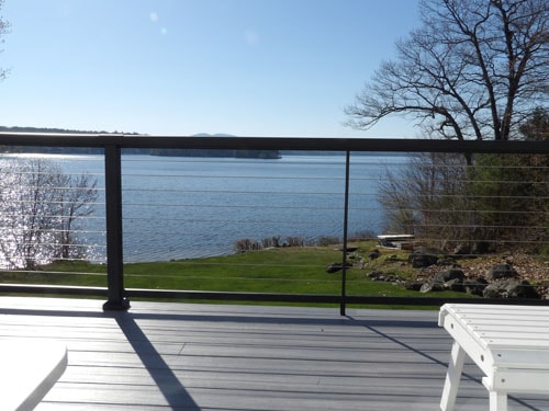 Gray composite deck with black cable railing and sweeping open lake view on a clear spring day