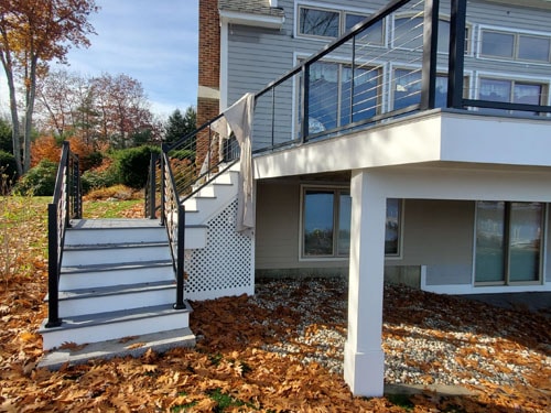 Black metal staircase with cable railings leading to elevated white deck with lattice skirting in fall foliage