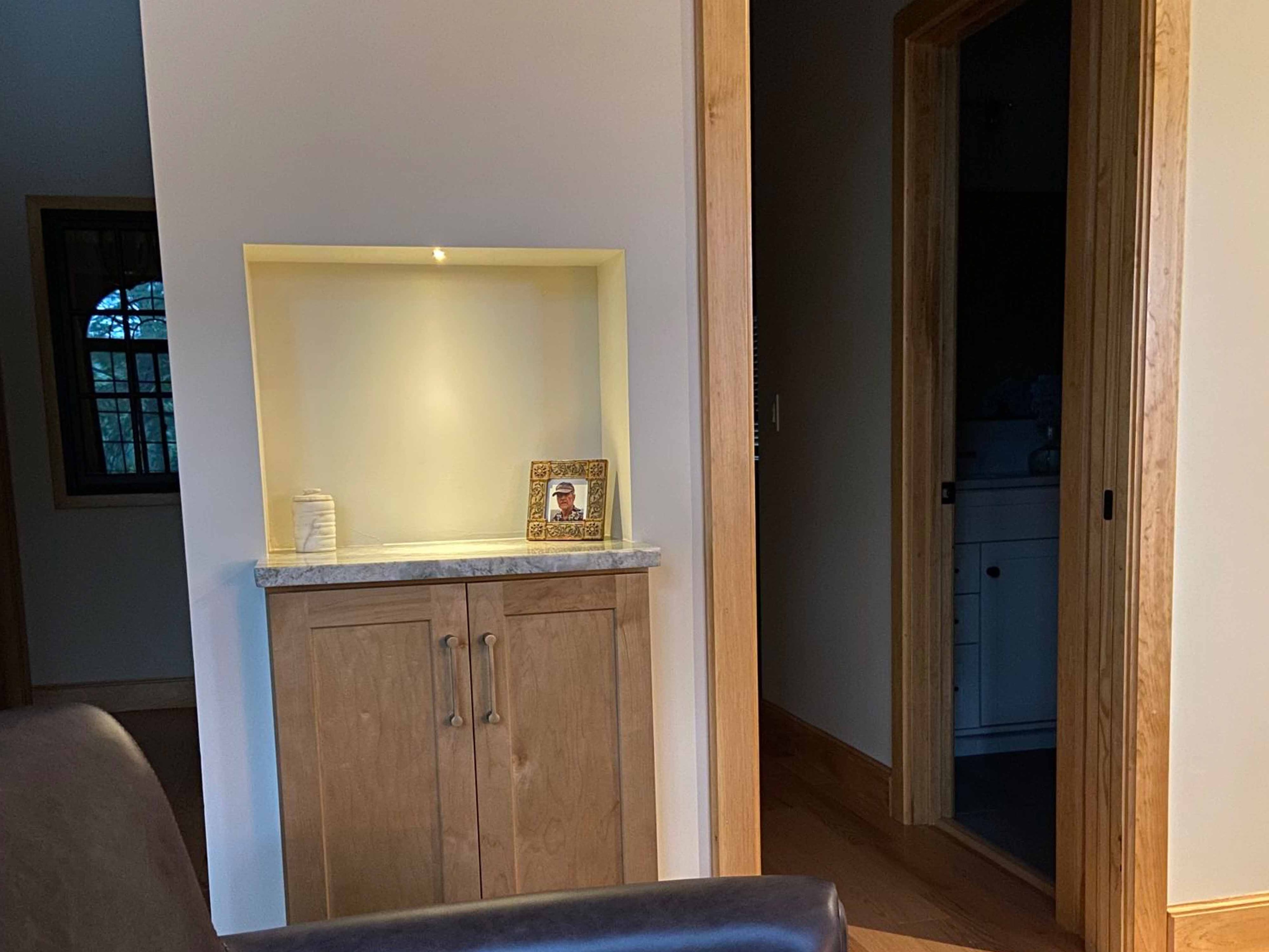 Custom built-in cabinet with lighted display niche, marble countertop, and natural wood trim framing a hallway to a white-painted laundry room