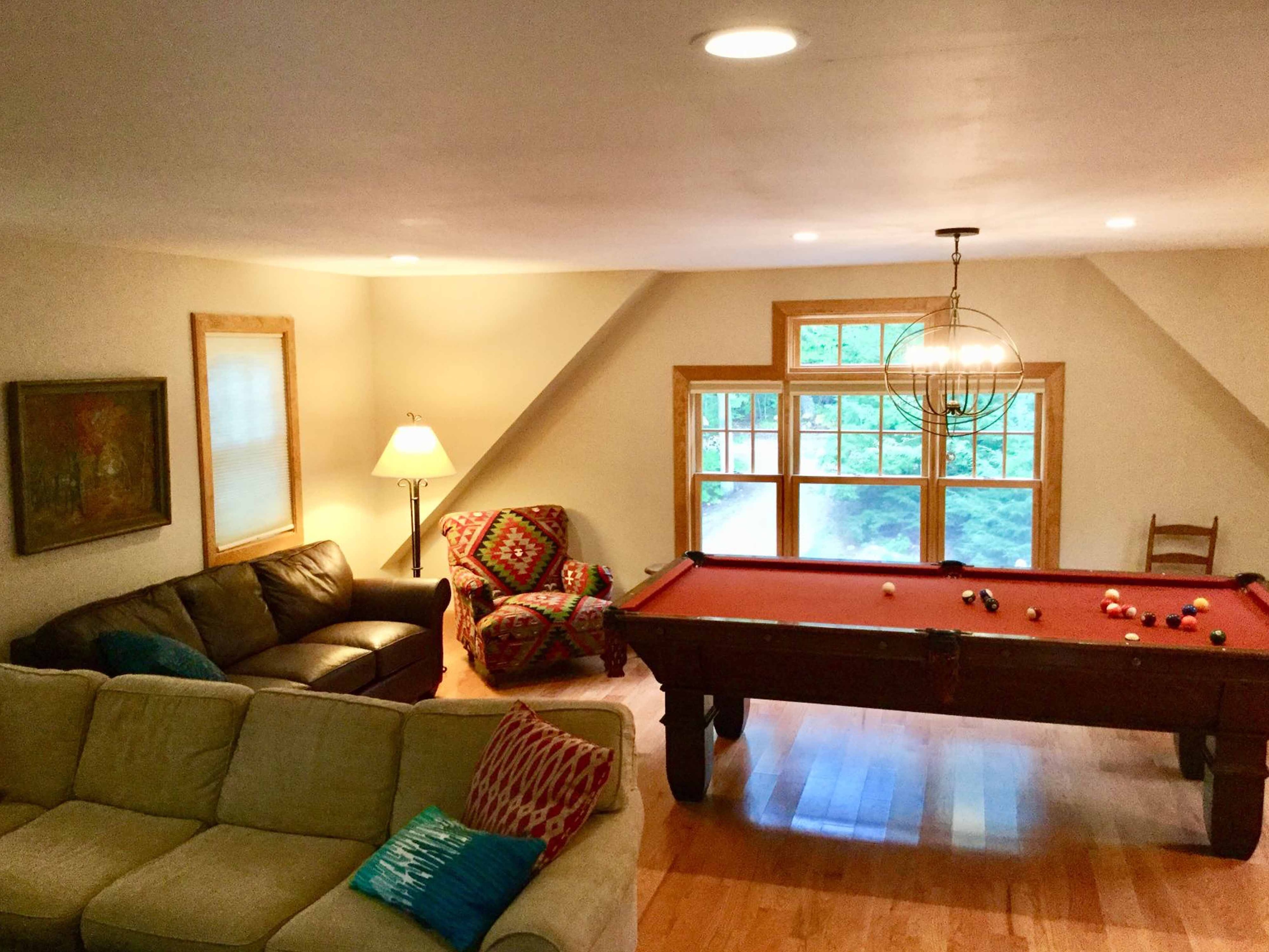 Finished bonus room with pool table, leather sectional, colorful accent chair, orb chandelier, and hardwood flooring under a sloped ceiling
