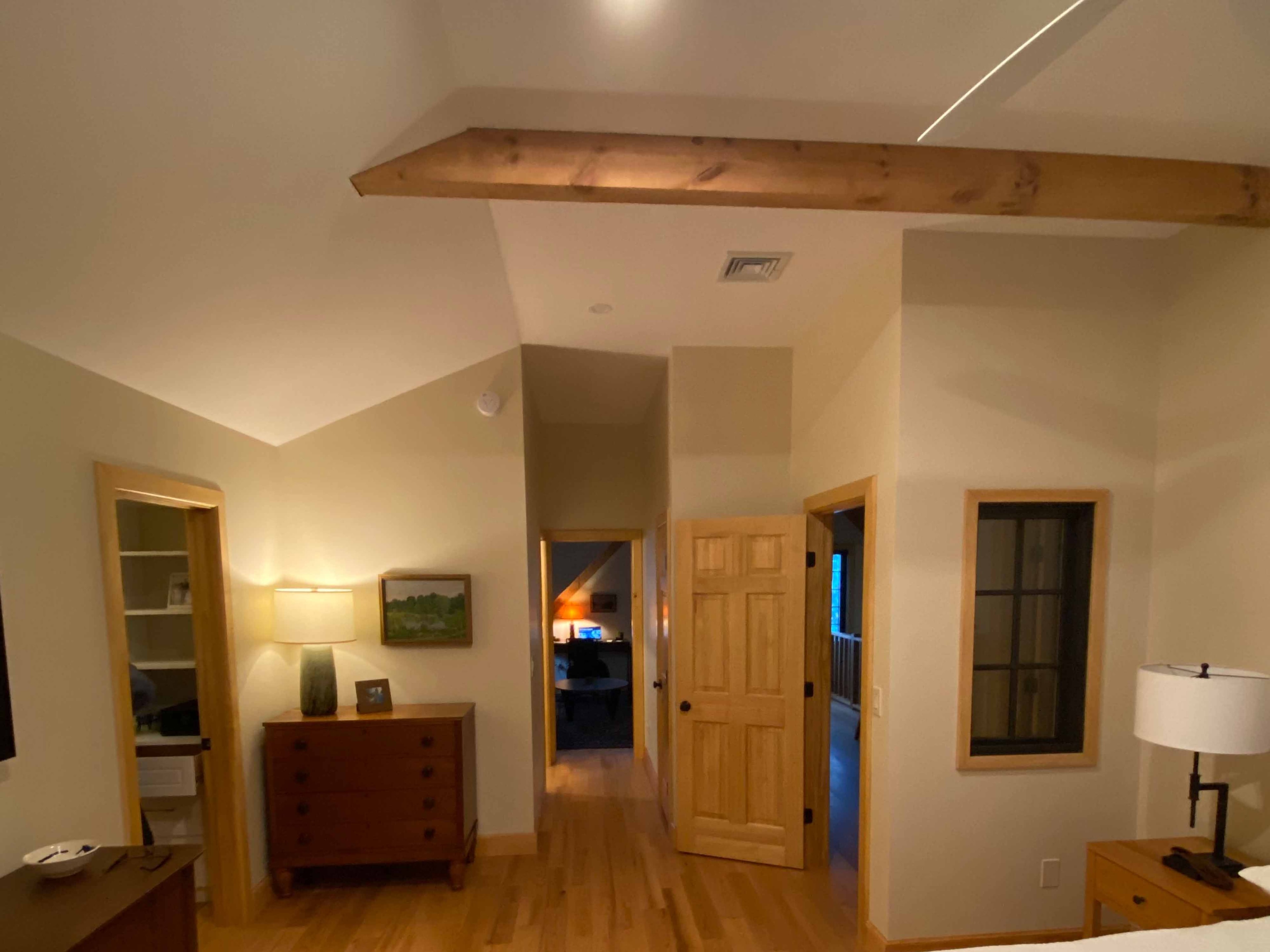 Finished master bedroom with vaulted ceiling, exposed knotty pine beam with LED cove lighting, natural wood trim doors, and hardwood flooring
