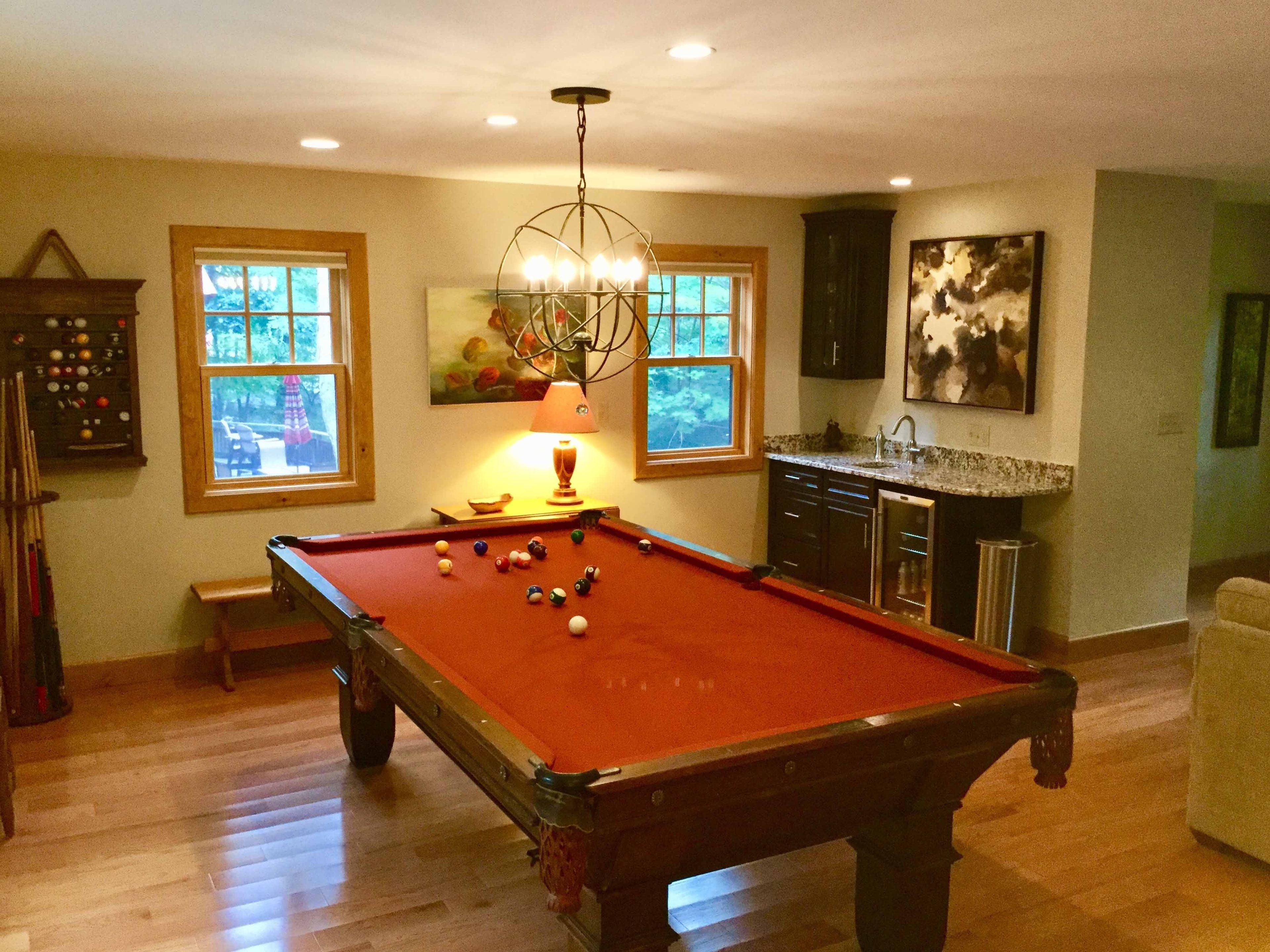 Full view of finished bonus room with pool table, orb chandelier, wet bar with granite countertop, hardwood flooring, and natural wood window trim