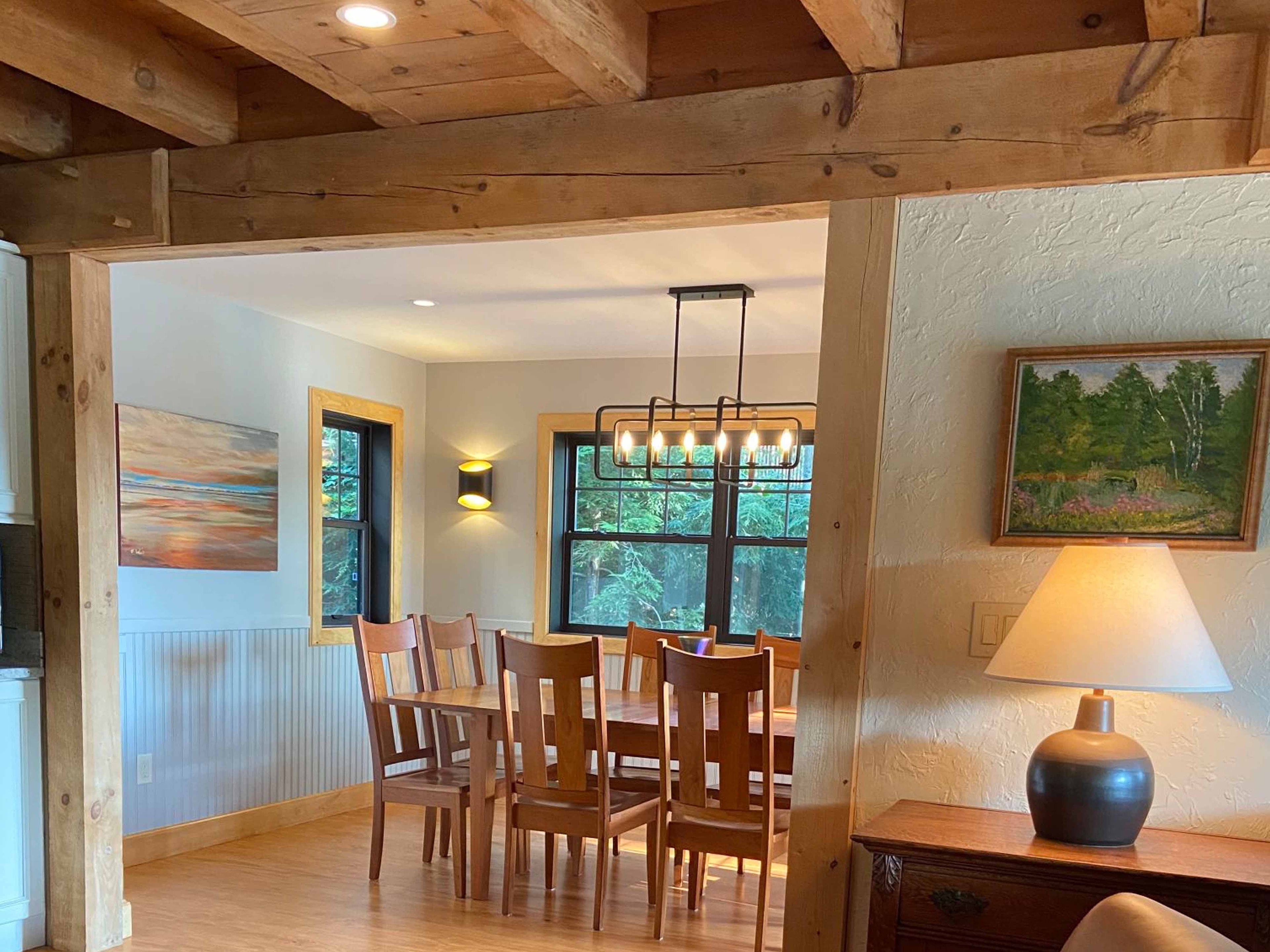 Finished dining room framed by heavy timber post-and-beam construction with knotty pine ceiling, modern linear chandelier, and black-framed windows