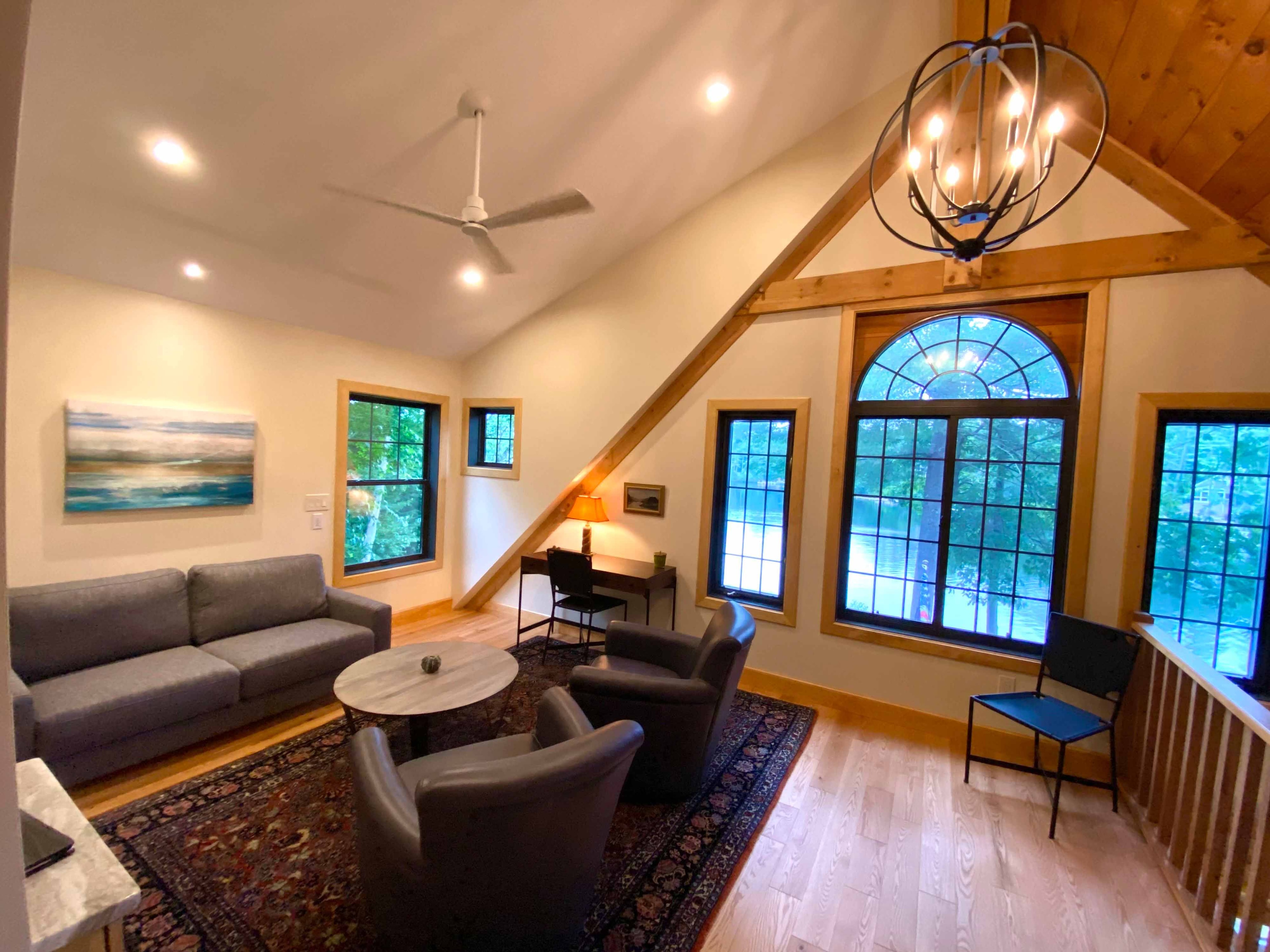 Finished loft living area with cathedral knotty pine ceiling, timber-frame knee braces, arched Palladian window, orb chandelier, and hardwood flooring