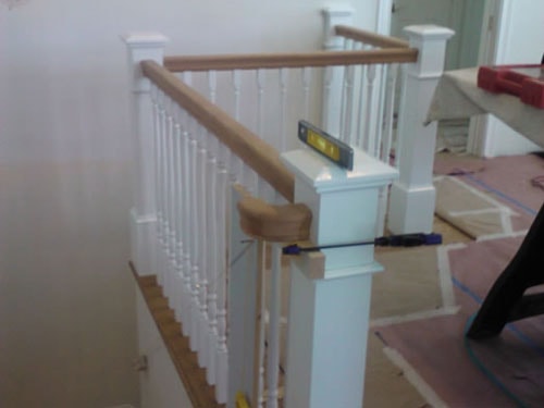 Stair railing installation in progress with white painted balusters, oak handrail, newel post, and level tool on top