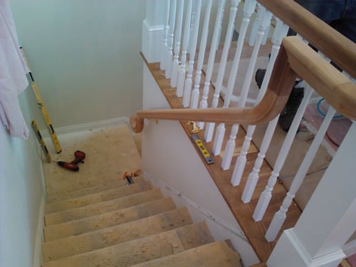 Staircase looking down showing white painted spindles, oak handrail with curved volute, and unfinished treads awaiting flooring