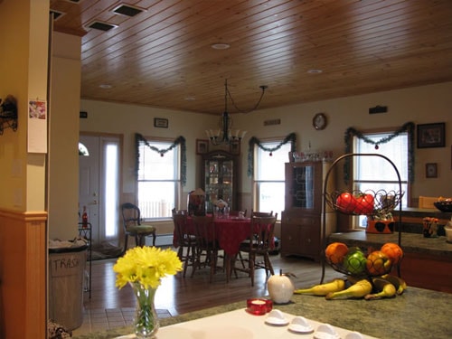 Dining room viewed from kitchen with knotty pine ceiling, holiday garland on windows, granite countertop in foreground, and maple hardwood flooring