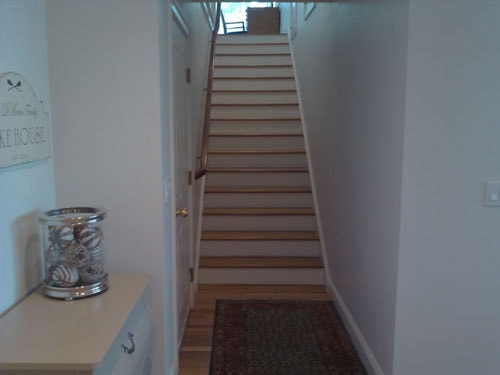 Finished lake house entry hallway with oak stair treads, white risers, painted wainscoting, hardwood floor, and decorative Lake House sign