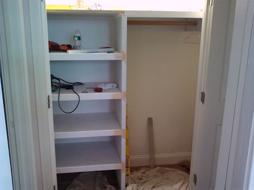 Built-in closet organizer under construction with white painted shelves, hanging rod, bifold door track, and tools on shelves