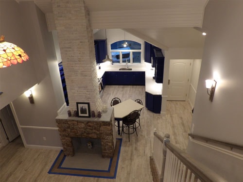 Bird's-eye view from loft down to open-plan kitchen and dining area with cobalt blue cabinets, stone chimney column, Tiffany lamp, and LVP flooring