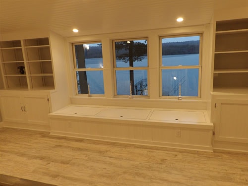 Close-up of full-width built-in window seat with storage lids and flanking white bookcases overlooking frozen lake through triple windows