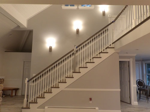 Dramatic straight-run staircase with white turned balusters, dark oak handrail, wainscoting, and three matching wall sconces in two-story open foyer