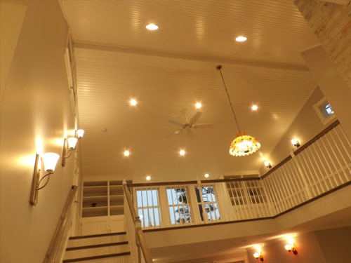 Cathedral beadboard ceiling with recessed lighting, ceiling fan, and Tiffany pendant chandelier viewed from loft level with oak railing in foreground