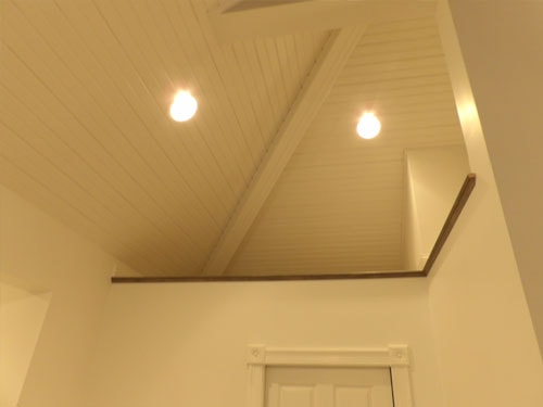 Vaulted beadboard ceiling detail with recessed lighting, dark oak railing cap, and white painted walls at stair landing