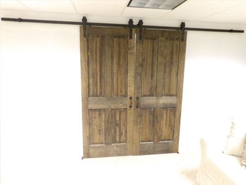 Custom double barn doors with dark walnut stain, raised panel detail, and black wrought-iron sliding hardware on black track — closed position