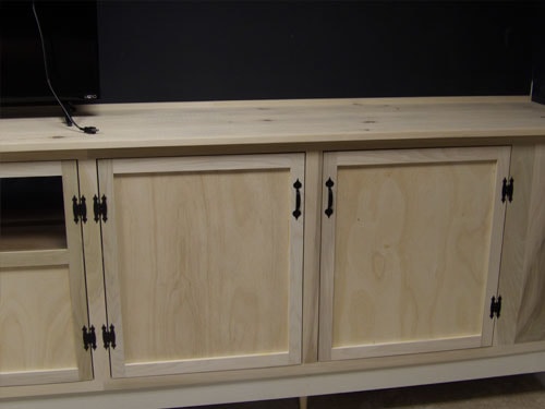 Close-up of right section of custom maple media cabinet showing raised panel doors, black bin-pull hardware, and butcher-block top