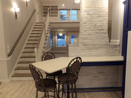Finished dining nook with white quartz peninsula countertop, cobblestone chimney column, straight-run staircase with white balusters, and loft railing at dusk