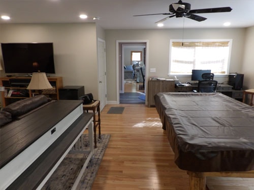 Rec room with covered pool table awaiting felt installation, TV wall with oak console, home office doorway, and oak hardwood flooring throughout