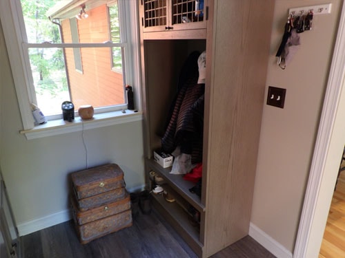 Built-in mudroom locker with open cubby, pull-out shoe shelf, upper storage cabinet with wire basket, key hooks on wall, and LVP flooring