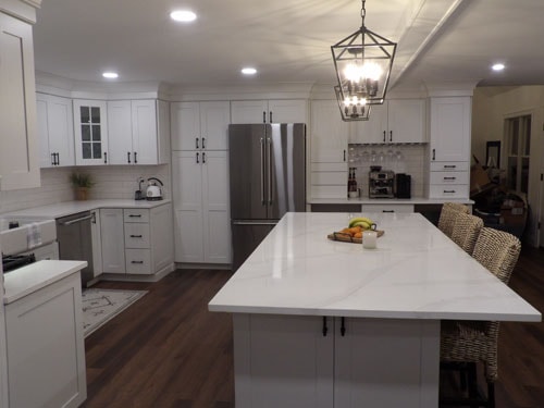Finished white shaker kitchen remodel with quartz waterfall island, stainless French door refrigerator, lantern pendant chandelier, subway tile backsplash, and dark hardwood flooring