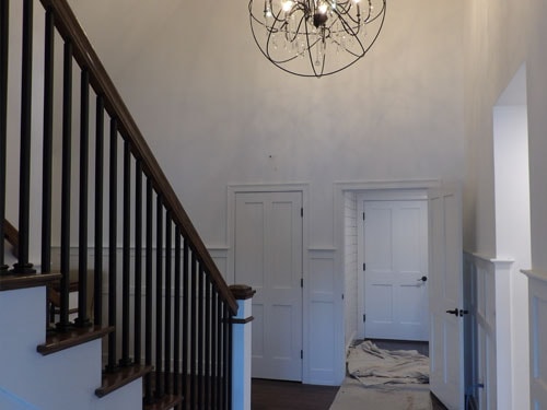 Two-story foyer with dark oak stair railing, square black balusters, wainscoting panel walls, six-panel doors, and orb chandelier