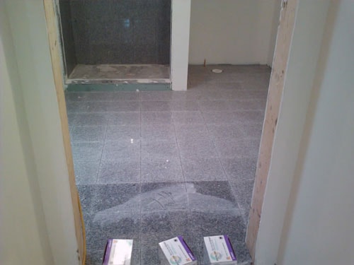 Gray granite tile flooring installation viewed through doorway with shower area beyond