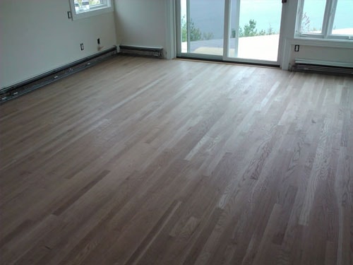 Finished light gray hardwood floor in bright open room with large windows and lake view