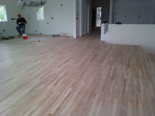Unfinished natural hardwood floor installation in open-plan room under construction with worker