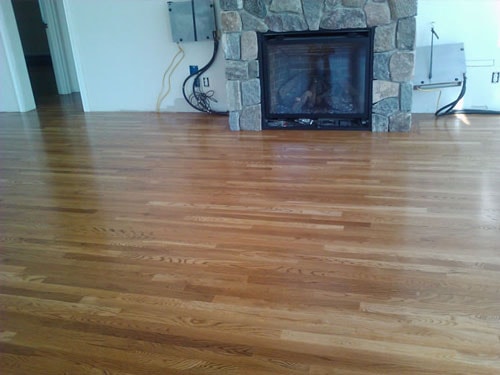 Completed warm oak hardwood floor with stone fireplace surround in residential living room