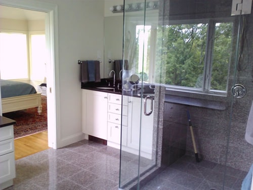 Master bathroom with gray tile floor, white vanity, dark granite countertop, and glass shower enclosure