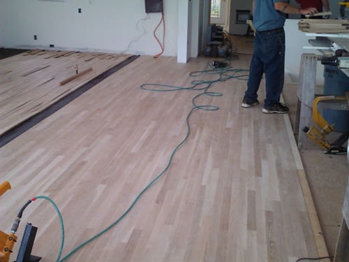 Worker standing on nearly complete unfinished hardwood floor installation in open room
