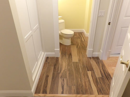 Wood-look porcelain tile floor in hallway leading to bathroom with yellow walls and white trim