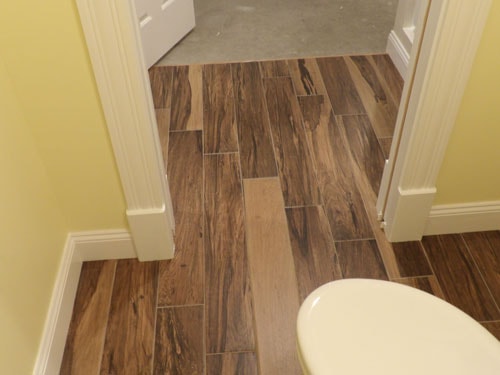 Close-up of wood-look porcelain tile floor in bathroom hallway with yellow walls and white baseboards