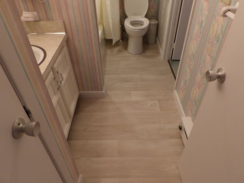 Light gray wood-look plank tile floor in bathroom with striped wallpaper and white vanity