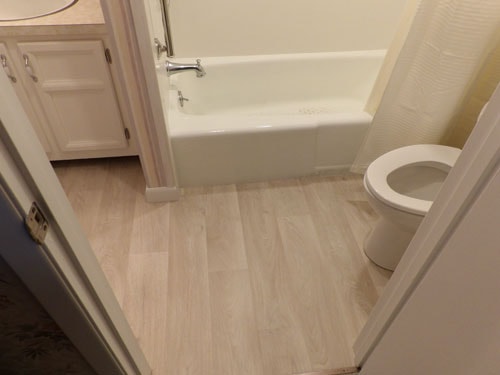 Light gray wood-look plank tile floor in bathroom with white soaking tub and toilet