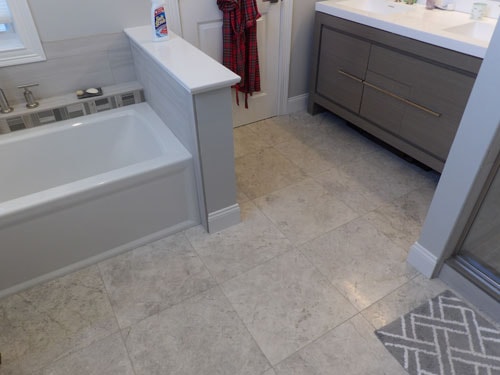 Large-format marble-look tile floor in master bathroom with soaking tub surround and gray vanity