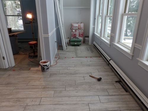 Wood-look porcelain tile installation in sunroom hallway from second angle showing tile materials and windows