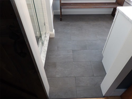 Charcoal slate tile bathroom floor from second angle showing glass shower, dark vanity, and white trim