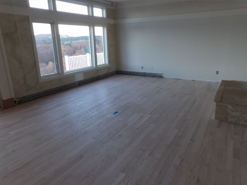 Unfinished white oak hardwood floor in large empty room with tall windows and fall foliage views