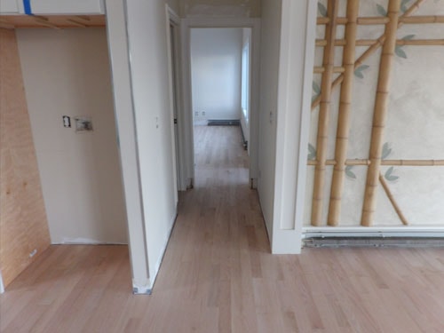 Unfinished white oak hardwood floor in hallway with bamboo wallpaper and white trim under construction