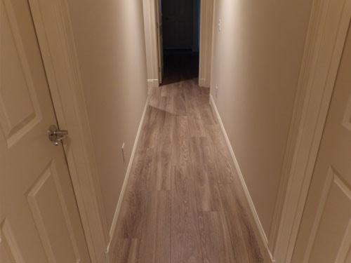 Gray LVP luxury vinyl plank flooring in narrow hallway with cream walls and white panel doors