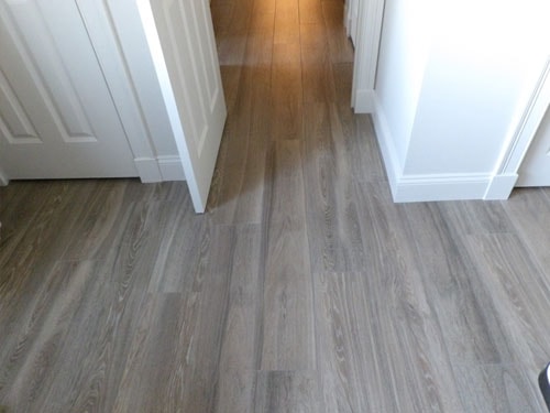 Gray LVP luxury vinyl plank flooring at hallway junction with white panel doors and white baseboards