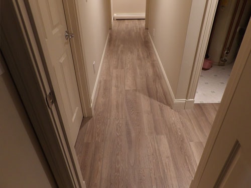 Gray LVP luxury vinyl plank flooring in hallway with white panel doors and glimpse of tile bathroom floor