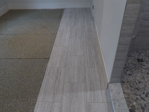 Light gray linear tile transition strip between carpet and pebble tile in bathroom doorway