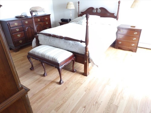 Light natural oak hardwood floor in bedroom with four-poster mahogany bed and matching dresser